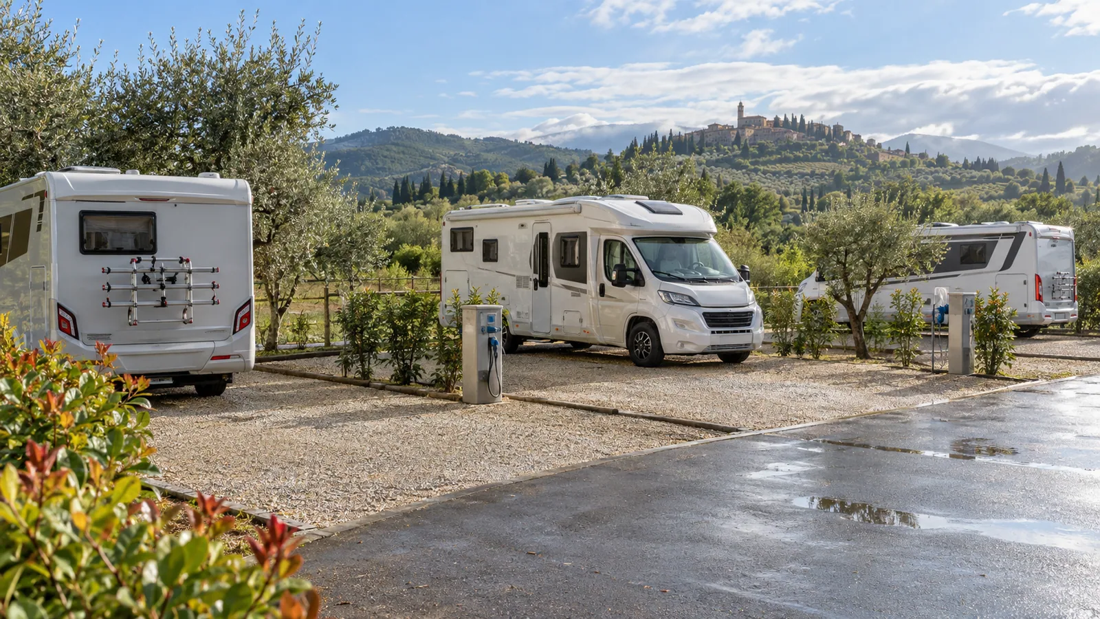 Area sosta camper con piazzole ordinate, colonnine di servizio e un paesaggio verde sullo sfondo.